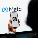 Hands holding smartphone with Meta Threads logo on screen, Meta branding in background.
